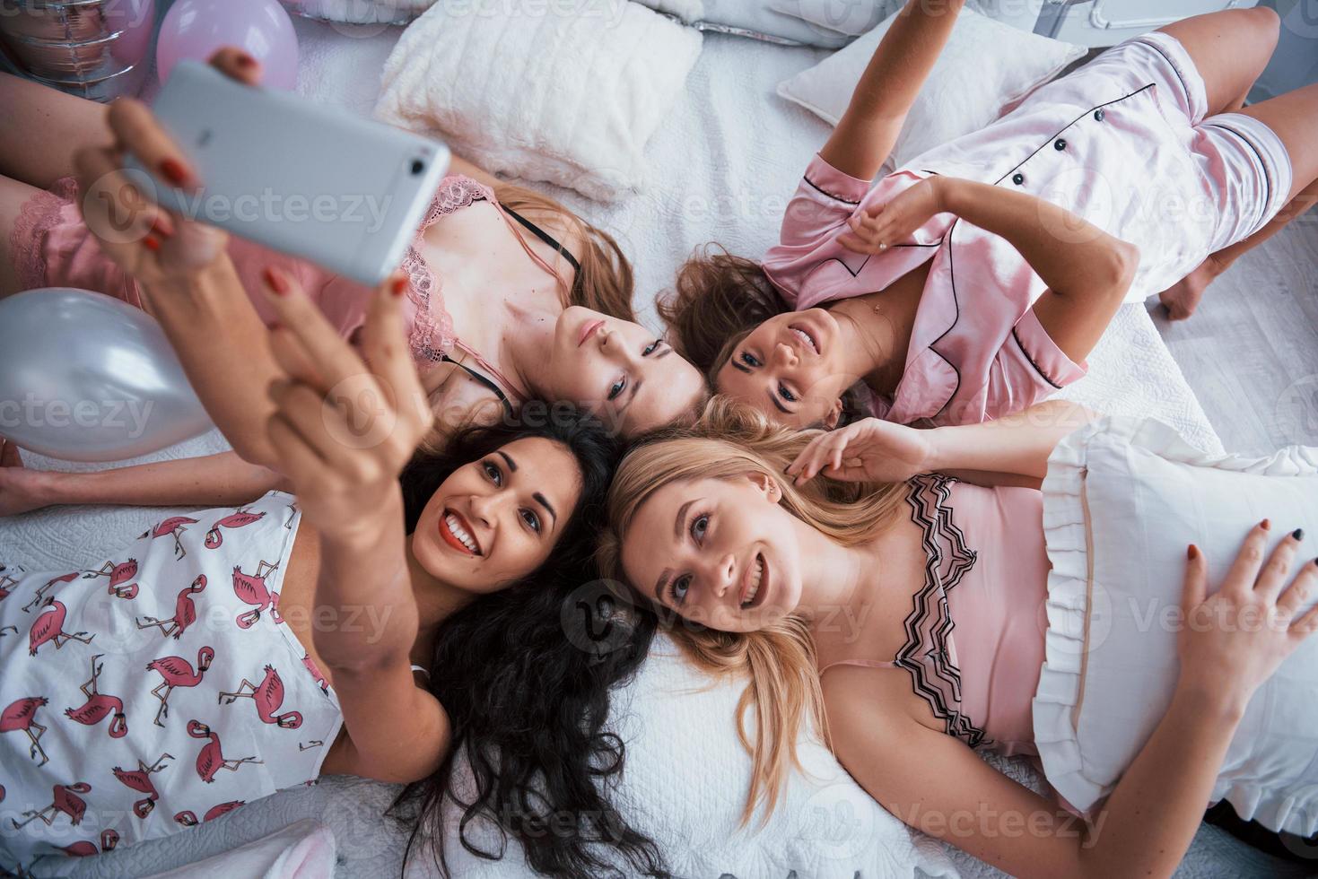 fare selfie con gli amici sdraiati sul letto all'addio al nubilato foto