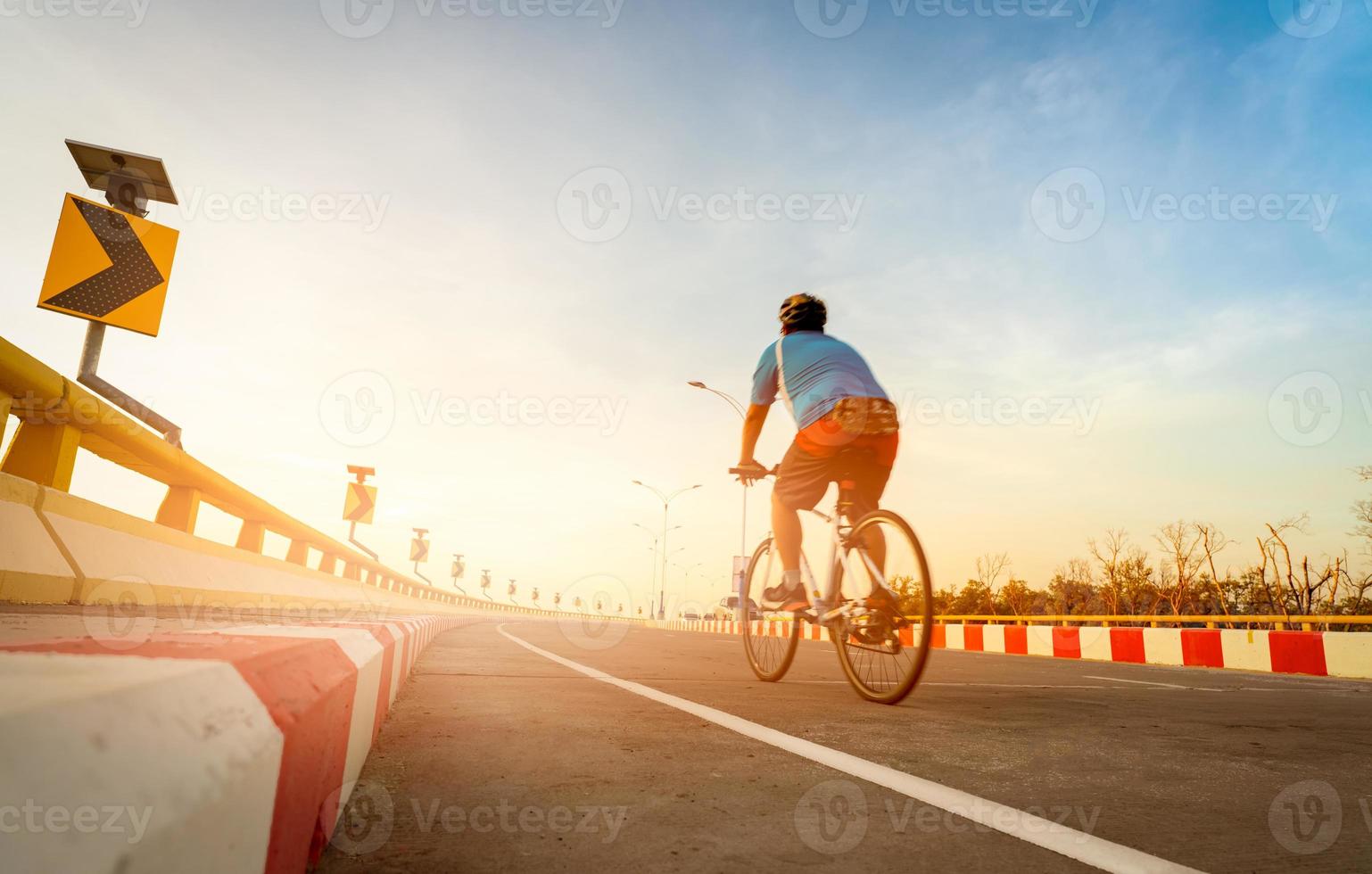 sfocatura vista posteriore di un uomo indossare il casco andare in bicicletta per l'esercizio. segnale stradale di curva con persone in bicicletta sulla strada. attività all'aperto in estate. uno stile di vita sano. sport e attività. foto
