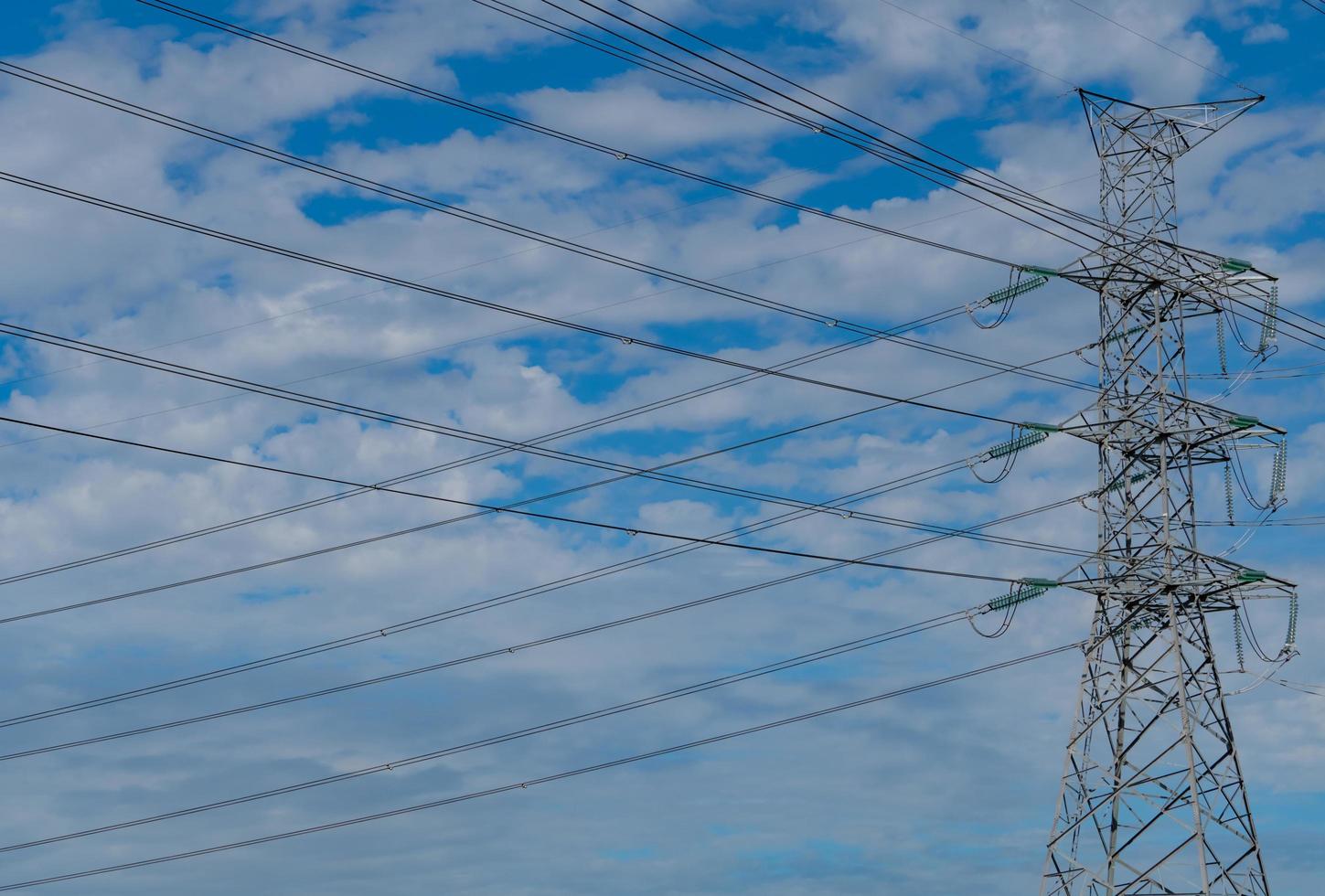 pilone elettrico ad alta tensione e filo elettrico contro il cielo blu e nuvole. vista dal basso del traliccio elettrico. torre di griglia ad alta tensione con cavo metallico. linee di trasmissione su torre di rete ad alta tensione. foto