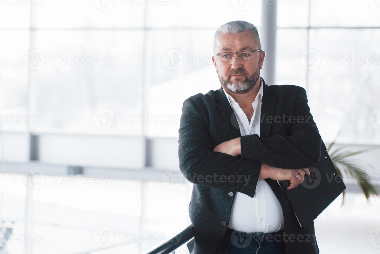 l'uomo serio aspetta i dipendenti. foto di uomo d'affari senior nella spaziosa stanza con piante dietro. detenzione e lettura di documenti