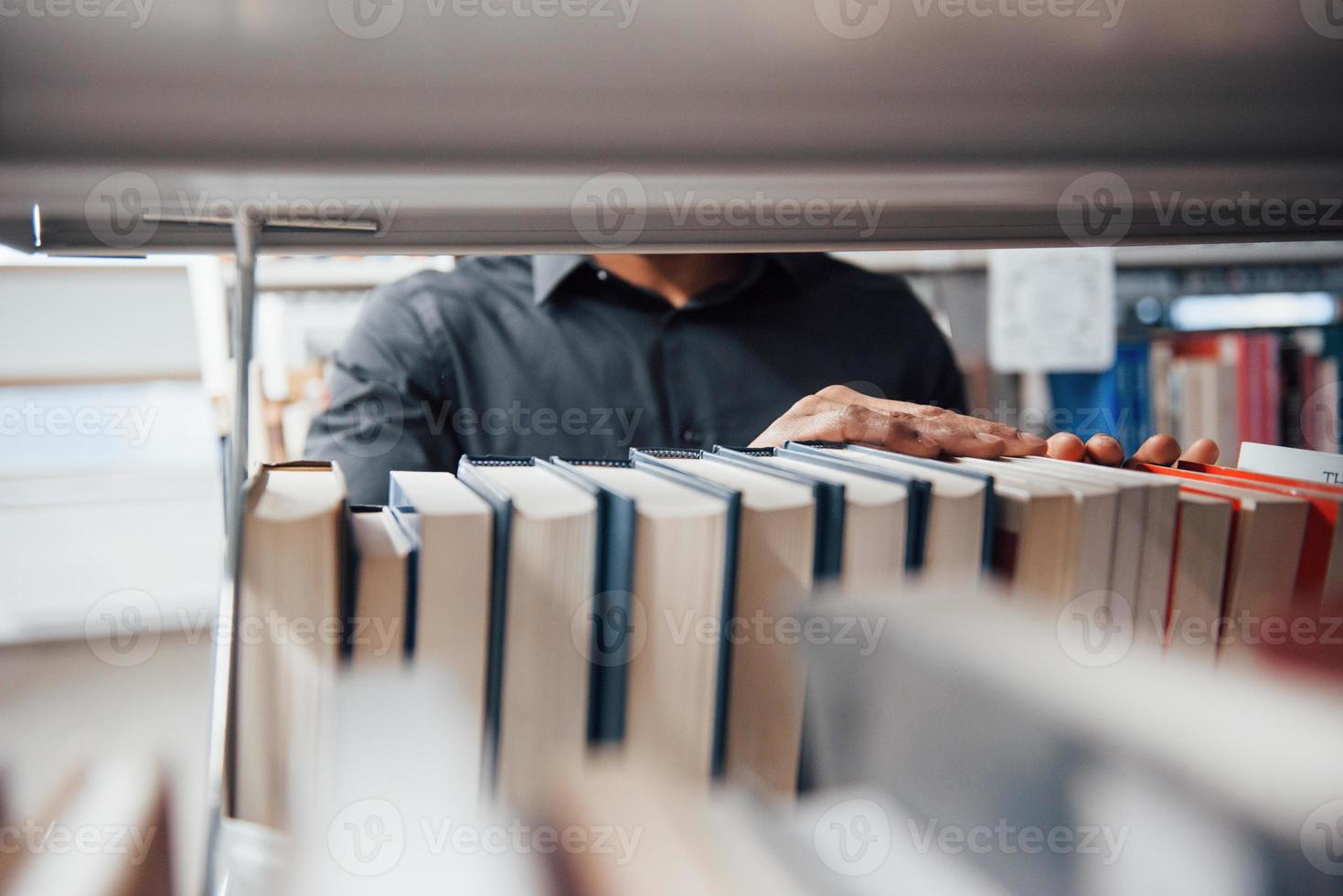 vista dettagliata. uomo afroamericano in biblioteca alla ricerca di alcune informazioni nei libri foto