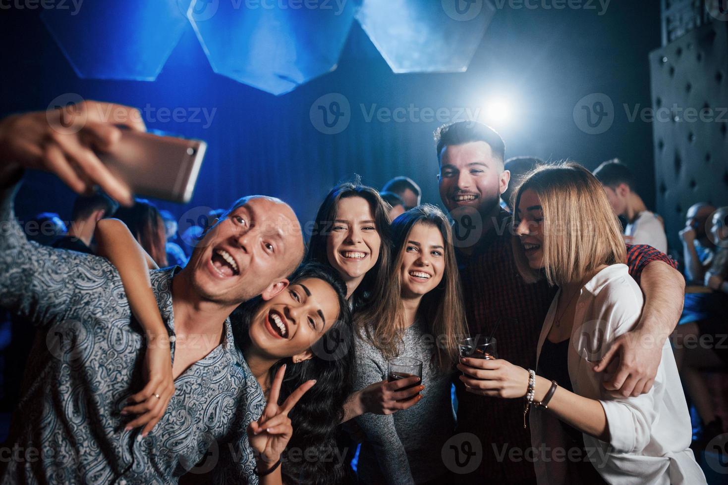 prenditi un momento per una foto. amici che prendono selfie in una bellissima discoteca. con le bevande in mano foto