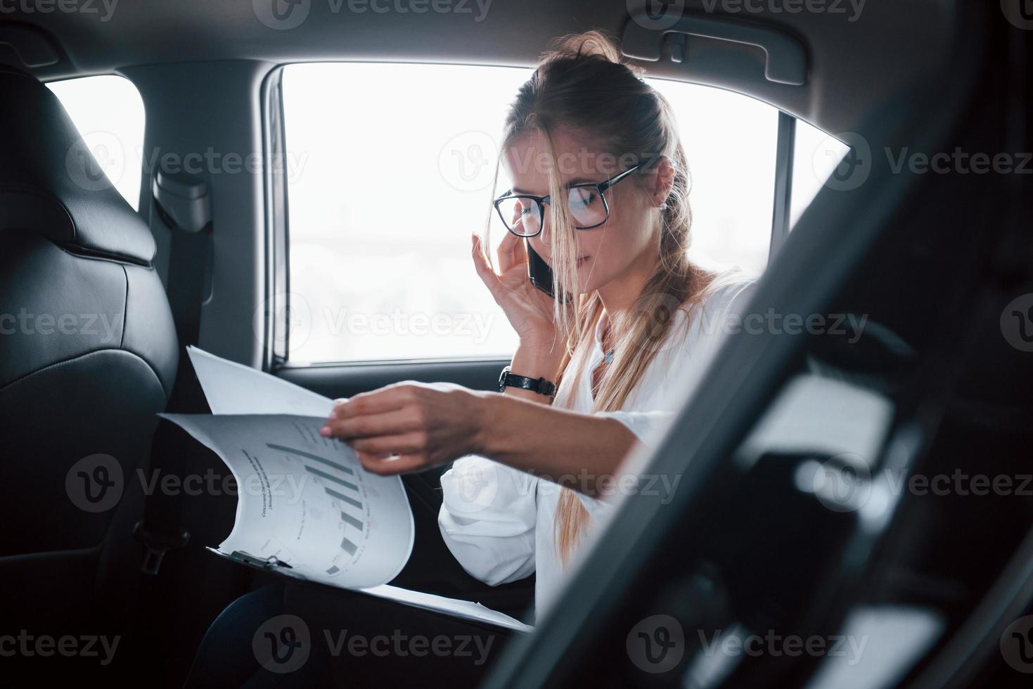 comunicazione con il capo. la donna d'affari intelligente si siede sul sedile posteriore dell'auto di lusso con interni neri foto