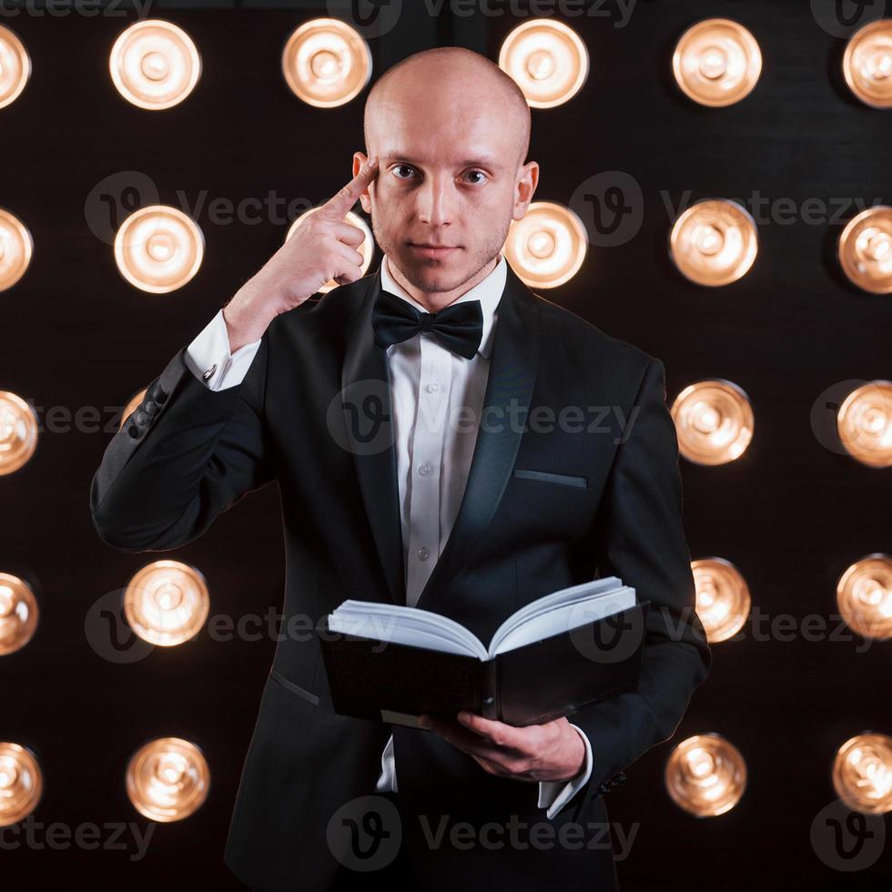 leggendo la tua mente. mago in abito nero in piedi nella stanza con un'illuminazione speciale nel backstage foto