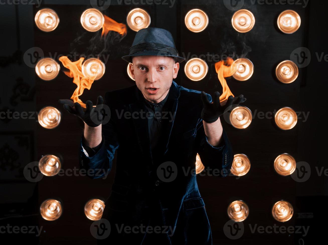 fiamme dalle mani. illusionista professionista in cappello nero, camicia e guanti che giocano con il fuoco foto