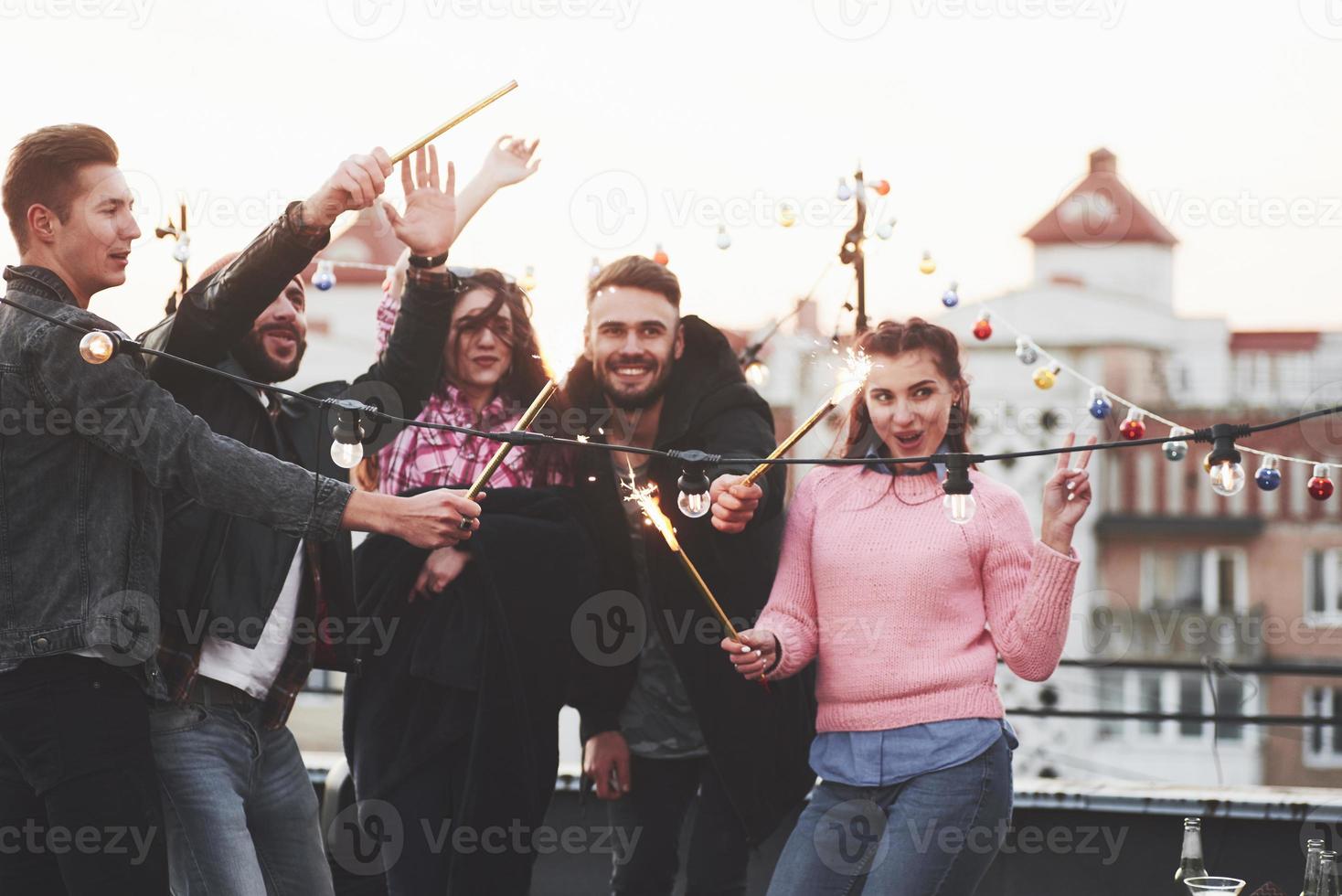 ragazza che mostra gesto per la foto. giocando con le stelle filanti sul tetto. gruppo di giovani bellissimi amici foto