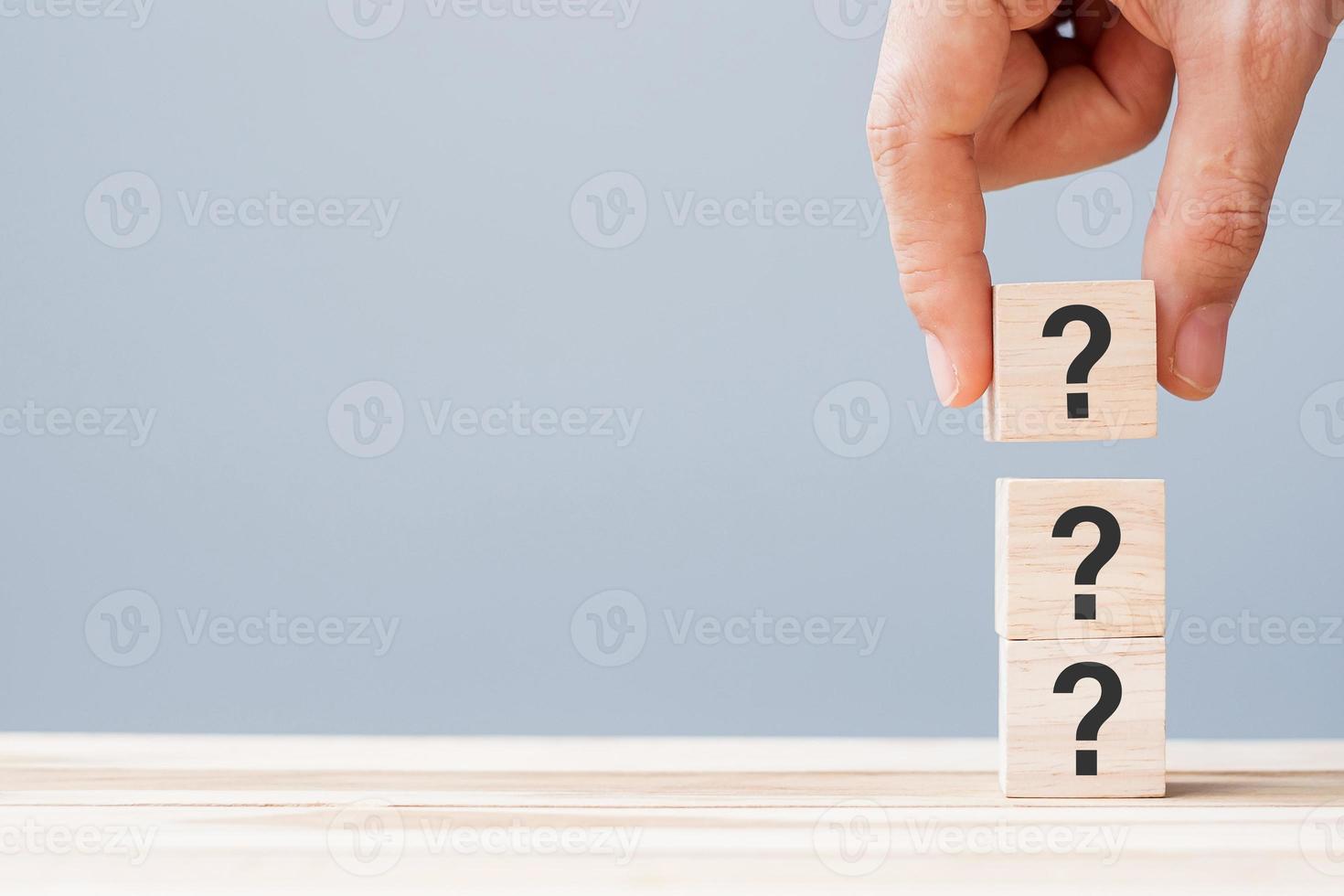 mano che tiene il punto interrogativo sul blocco di legno del cubo sullo sfondo del tavolo. faq, risposta, q e a, concetti di informazione, comunicazione e interrogazione foto
