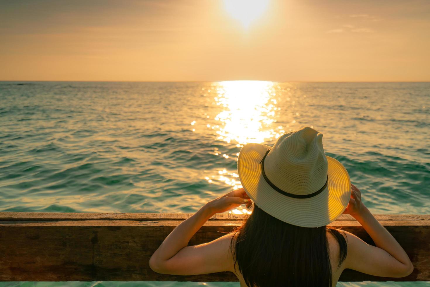 vista posteriore della donna asiatica sexy dei capelli lunghi neri con il cappello di paglia che si rilassa e si gode la vacanza sulla spiaggia del paradiso tropicale e guarda il cielo al tramonto. vacanze estive. viaggio di vacanza da solo. vibrazioni estive. foto