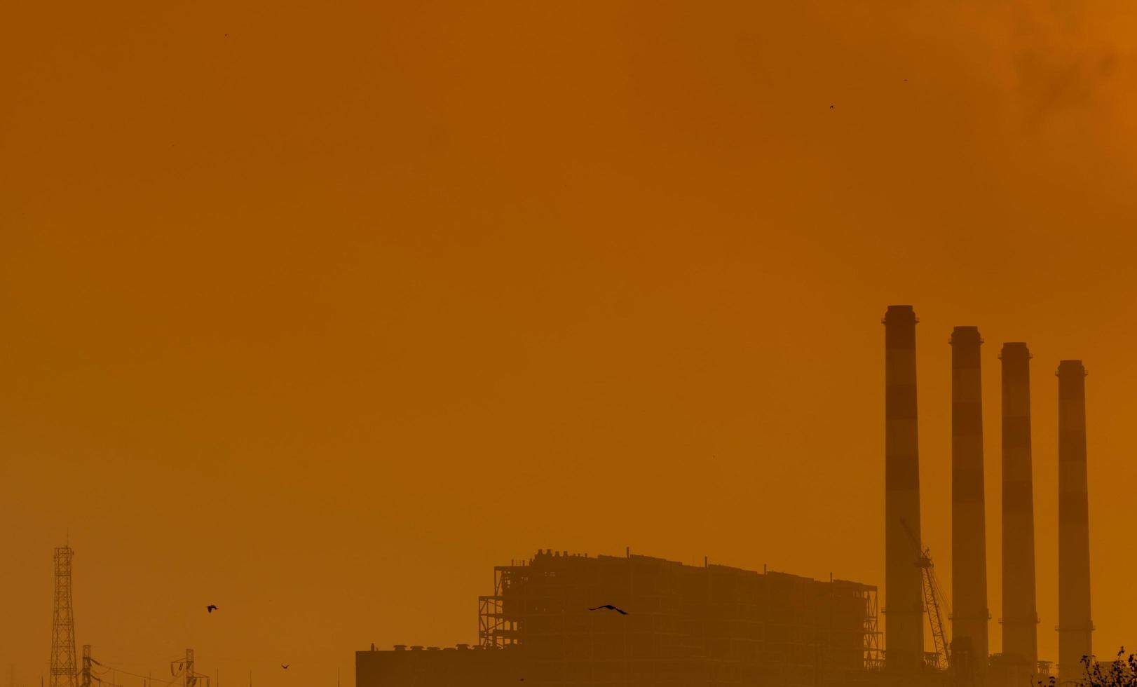 centrale elettrica con cielo al tramonto arancione e uccelli che volano nel cielo. concetto di inquinamento atmosferico. energia per fabbrica di supporto in zona industriale. potenza ed energia. polvere diffusa nell'aria la sera. foto