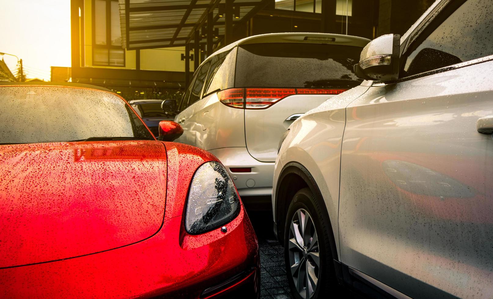 auto rossa e argento parcheggiata nel parcheggio esterno in cemento dell'hotel, della casa o dell'appartamento. tecnologia per auto elettriche o ibride. posto auto in affitto attività. gocce di pioggia su auto sportive e suv. foto