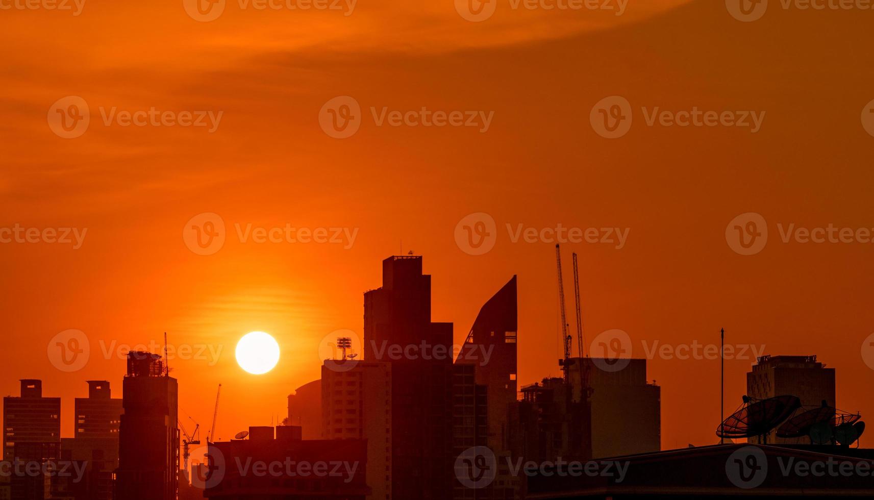 edificio d'affari nel centro cittadino al tramonto con un bel cielo al tramonto. sagoma di condominio e appartamento la sera. paesaggio urbano della costruzione del grattacielo e della gru di costruzione. grande sole con cielo rosso. foto