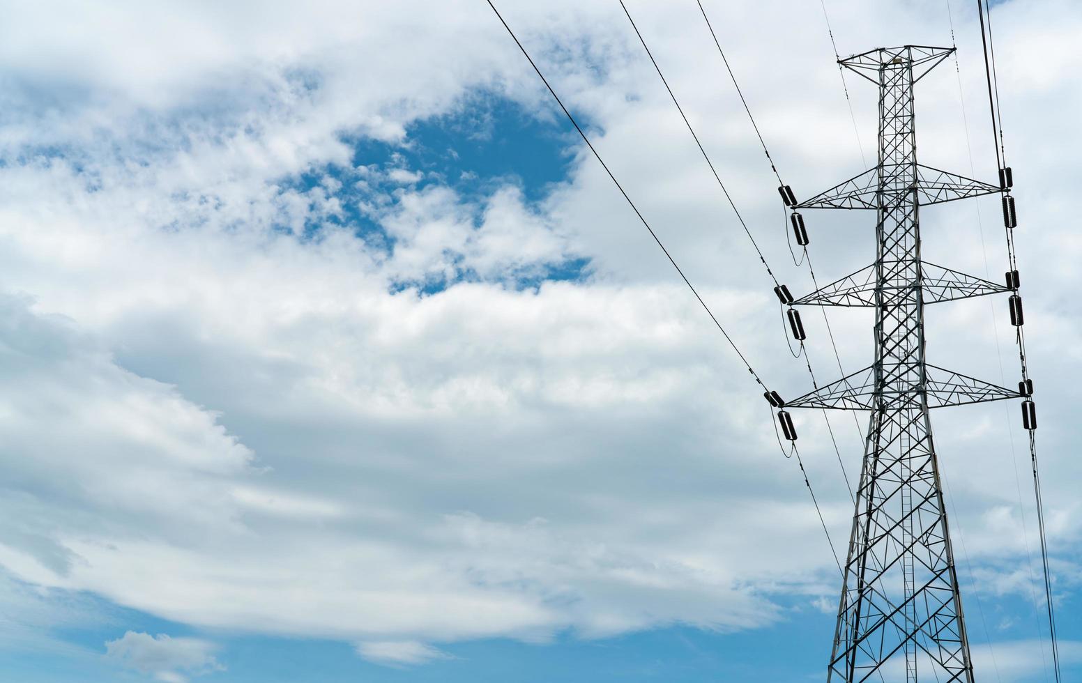 traliccio elettrico ad alta tensione e filo elettrico con cielo azzurro e nuvole bianche. palo elettrico alto. concetto di potenza ed energia. torre della griglia ad alta tensione con cavo metallico alla stazione di distribuzione. foto