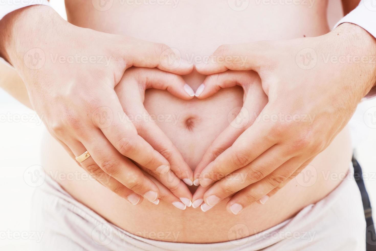 una coppia che fa con le mani a forma di cuore sulla pancia incinta foto
