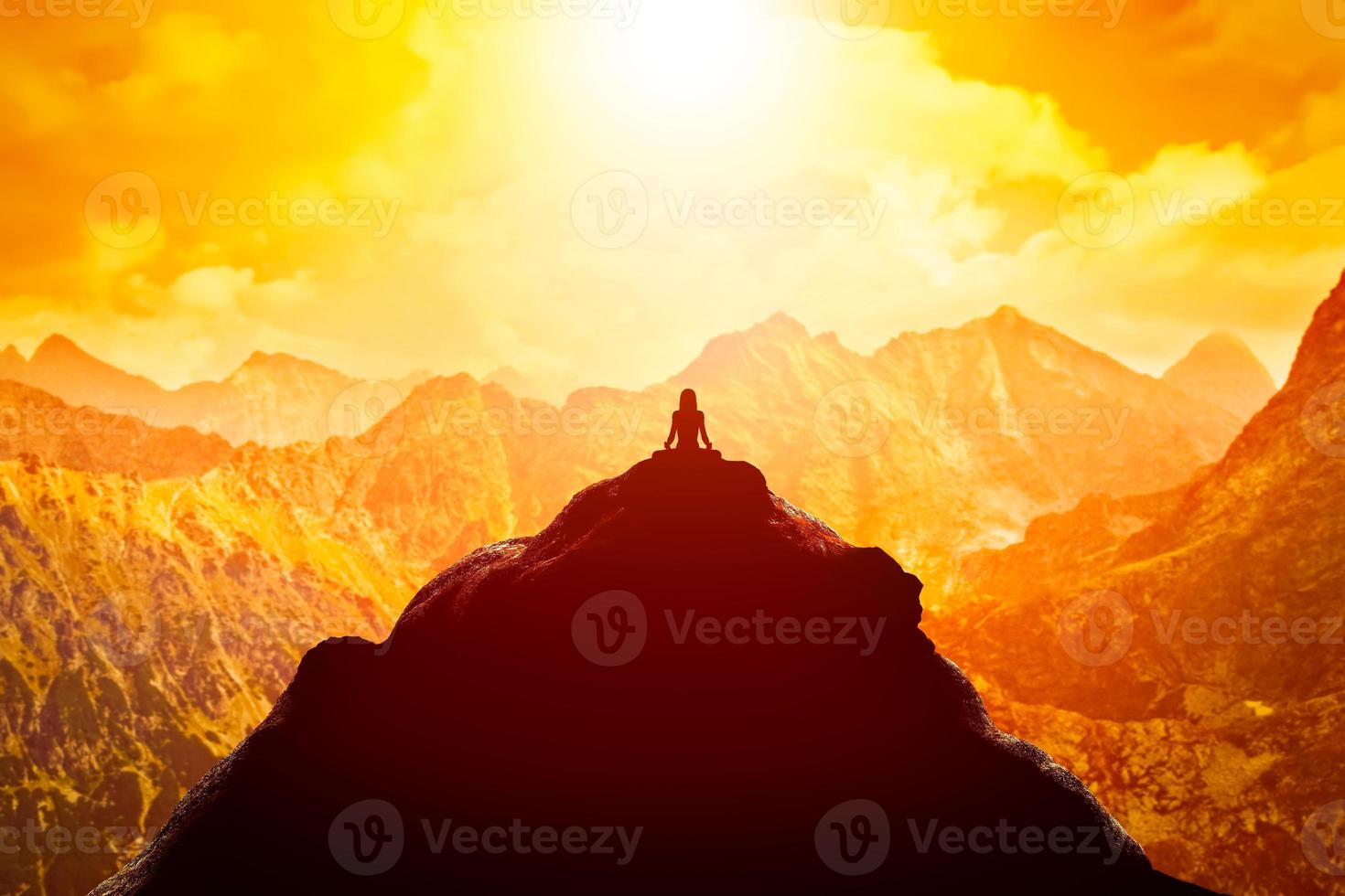 donna meditando in posizione yoga seduta sulla cima di una montagna sopra le nuvole al tramonto. foto