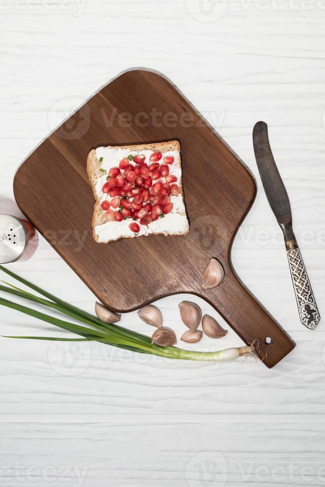 il pane ha crema di formaggio e melograno su sfondo bianco. foto