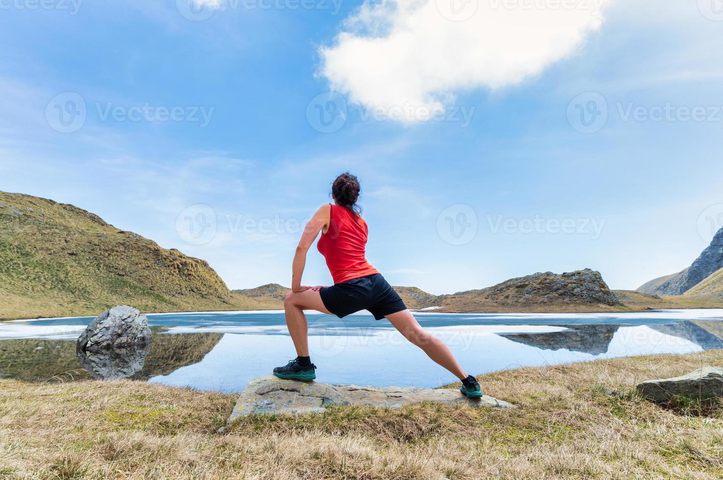 una giovane donna pratica ginnastica davanti a un laghetto alpino foto