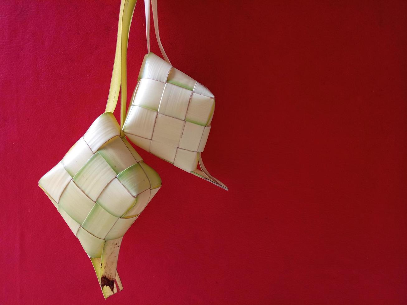 ketupat, gnocco di riso indonesiano su sfondo rosso. ketupat è un involucro di riso naturale a base di giovani foglie di cocco per la cottura del riso durante eid mubarak, eid ul fitr foto