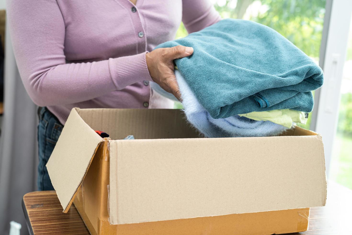 tenendo in mano una scatola per la donazione di vestiti con vestiti usati e una bambola a casa per sostenere l'aiuto ai poveri nel mondo. foto