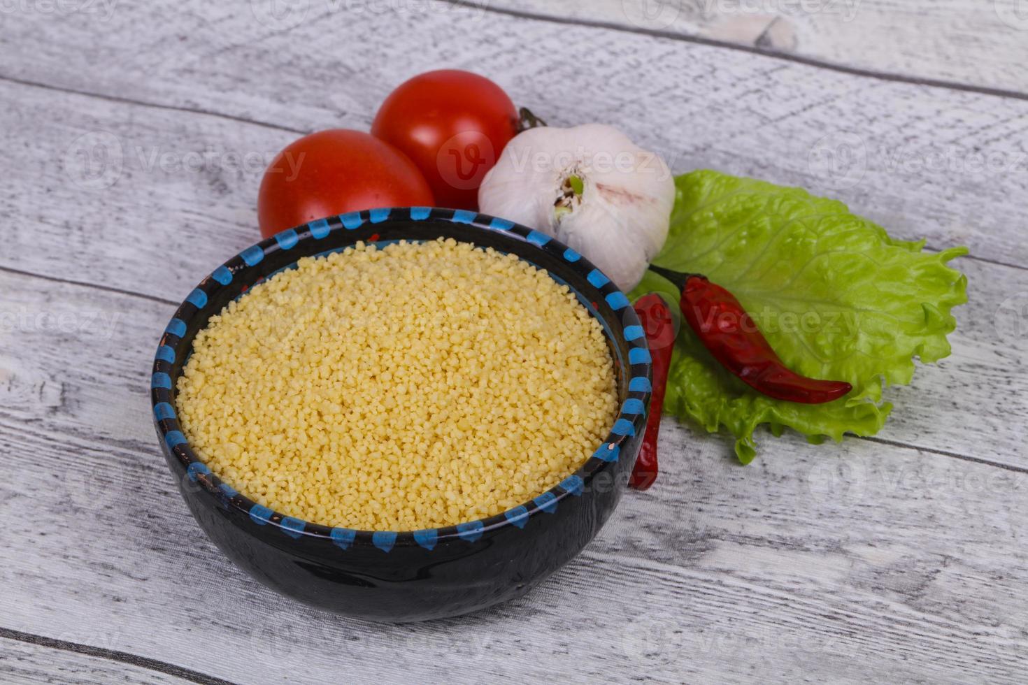 cous cous crudo nella ciotola servito con foglie di insalata, pomodoro e pepe foto