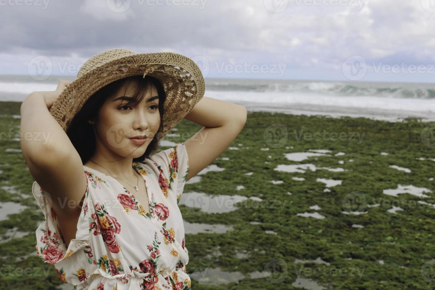 una giovane ragazza asiatica che indossa un cappello da spiaggia si sta rilassando sulla spiaggia del cielo blu a gunungkidul, in indonesia foto