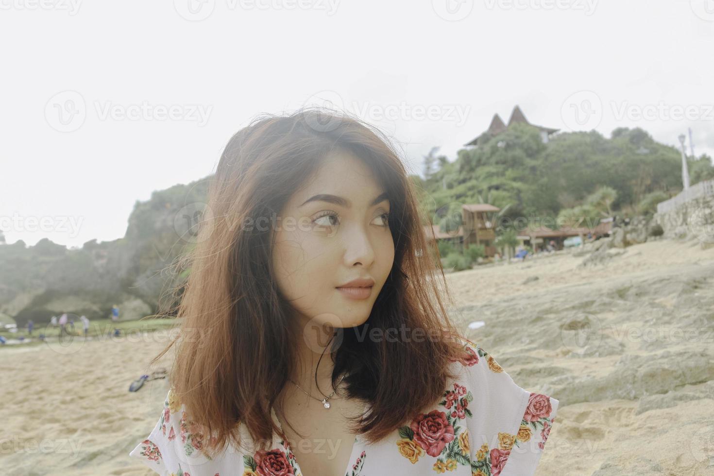 una giovane donna asiatica seduta e rilassante sulla spiaggia di sabbia, gunungkidul, indonesia foto