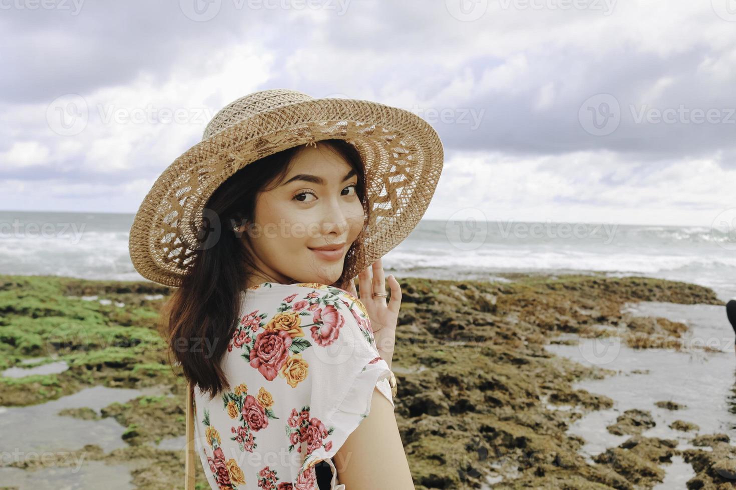 una giovane ragazza asiatica che indossa un cappello da spiaggia si sta rilassando sulla spiaggia del cielo blu a gunungkidul, in indonesia foto