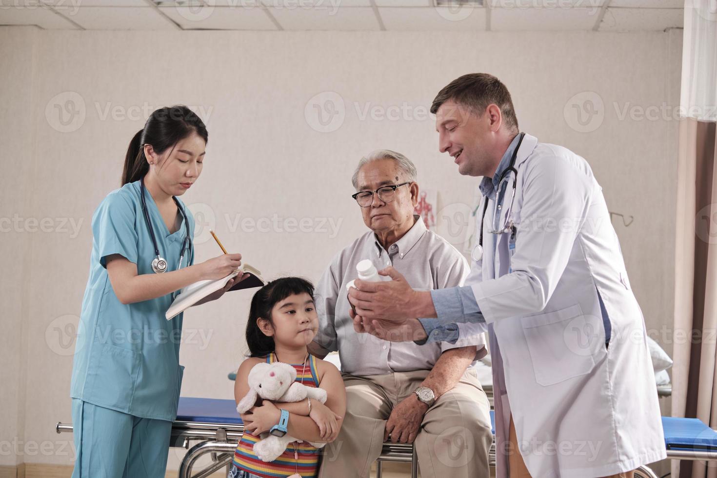 il medico maschio caucasico professionista consiglia il nonno e il nipote, spiega la prescrizione con i tirocinanti al letto d'ospedale del paziente, le consultazioni sulla malattia e la clinica per l'esame della salute della famiglia. foto