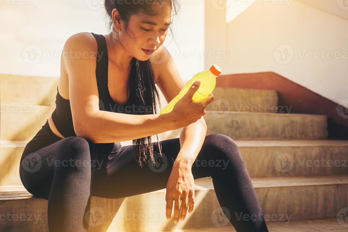 corridore stanco donna con una bottiglia di bevanda elettrolita freschezza dopo l'allenamento allenamento all'aperto presso le scale dello stadio. foto