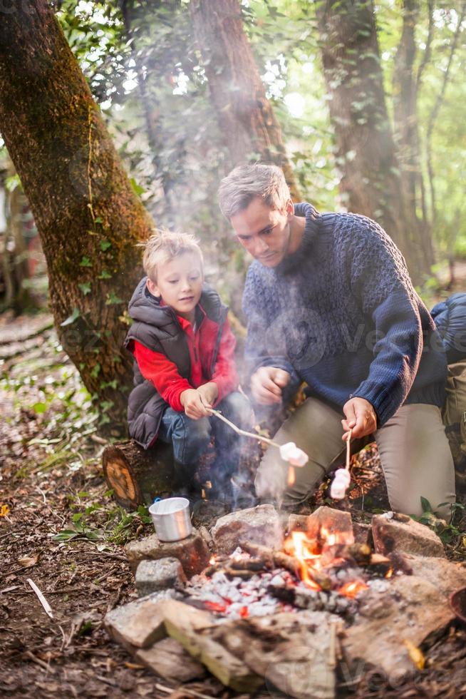 il padre e suo figlio arrostiscono i marshmallow su un fuoco foto