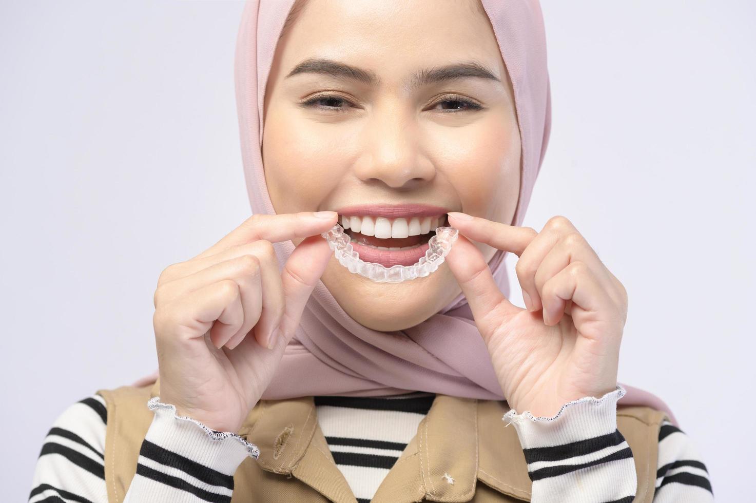una giovane donna musulmana che tiene bretelle invisalign in studio, assistenza sanitaria dentale e concetto ortodontico.. foto