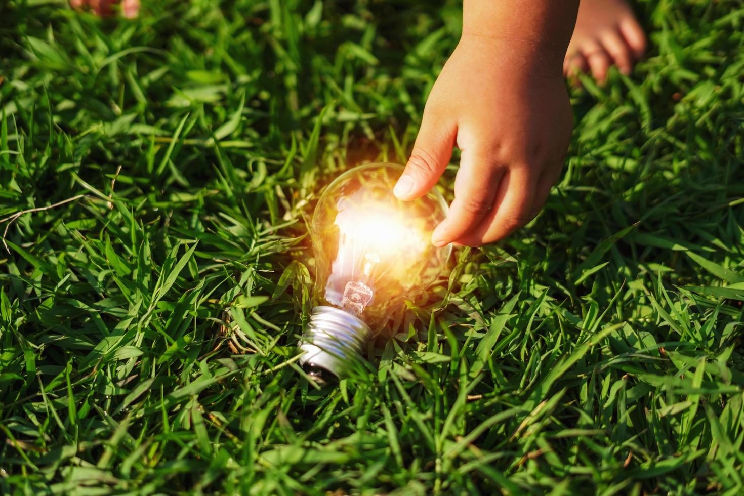 mano dei bambini che tiene la lampadina sull'erba verde. concetto di energia ecologica foto