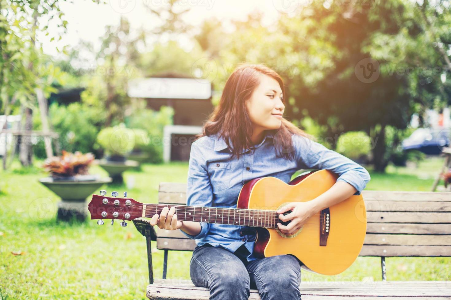 bella giovane donna che suona la chitarra seduta su una panchina, concetto di tempo felice. foto