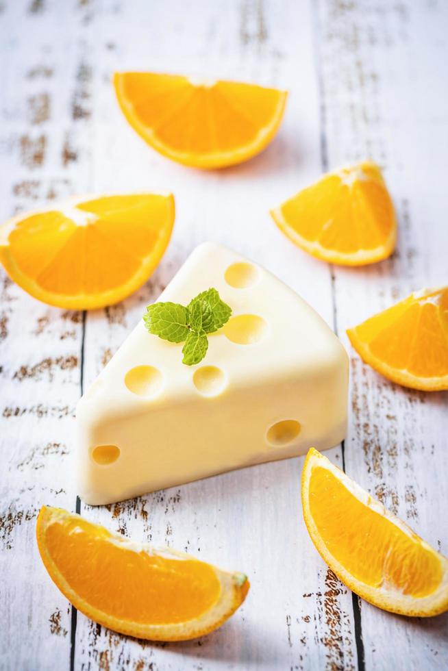 fatto in casa di torta al cioccolato bianco fresco a forma di fetta di formaggio putt su tavola di legno bianca e menta, arancia. concetto di cibo dolce e dessert. dolci decorati per le vacanze. vista ravvicinata del dessert. foto