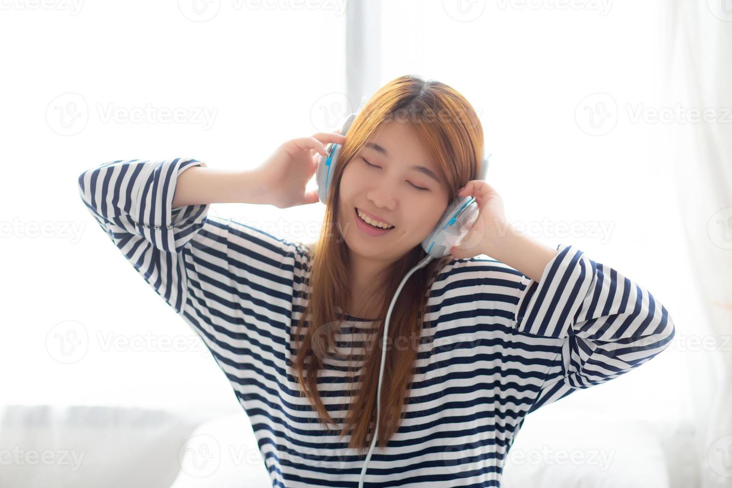 la bella giovane donna asiatica si diverte e si diverte ad ascoltare musica con la cuffia seduta in camera da letto, la ragazza si rilassa con il concetto di auricolare, tempo libero e tecnologia. foto