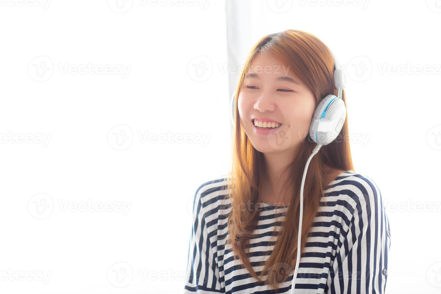 la bella giovane donna asiatica si diverte e si diverte ad ascoltare musica con la cuffia seduta in camera da letto, la ragazza si rilassa con il concetto di auricolare, tempo libero e tecnologia. foto