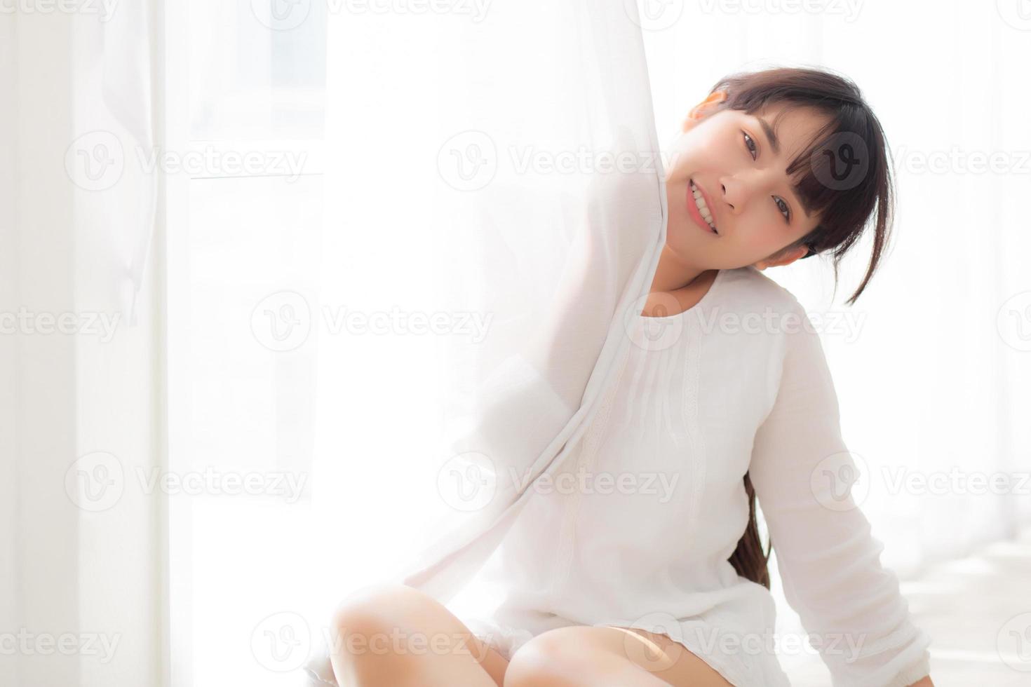 ritratto di bella giovane donna asiatica in piedi alla finestra e sorridere mentre si sveglia con l'alba al mattino, ragazza felice con freschezza e allegra, stile di vita e concetto di relax. foto