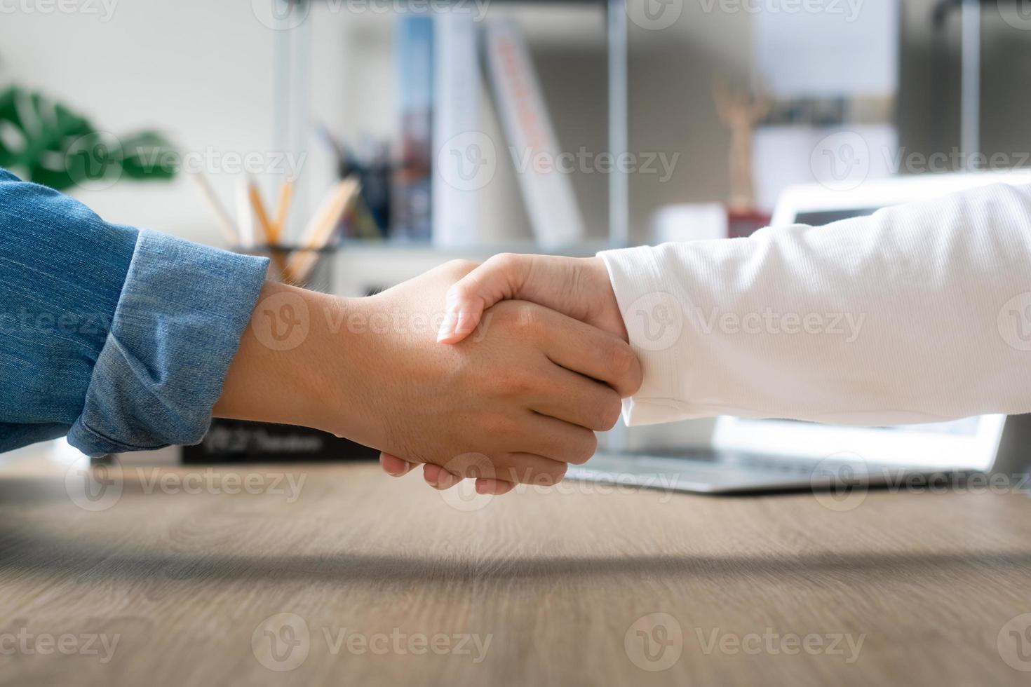 giovane uomo d'affari che stringe la mano a una cliente femminile a un tavolo da riunione in ufficio, raggiungendo un ottimo affare. foto