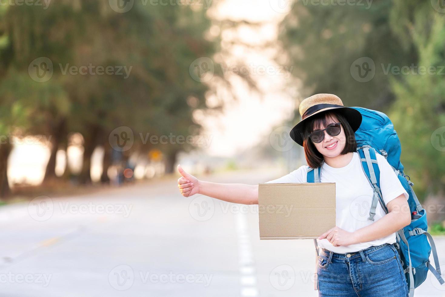 sorriso felice autostoppista donna asiatica zaino in attesa del trasporto in auto durante il fine settimana per il viaggio e il viaggio in vacanza all'ora del tramonto foto