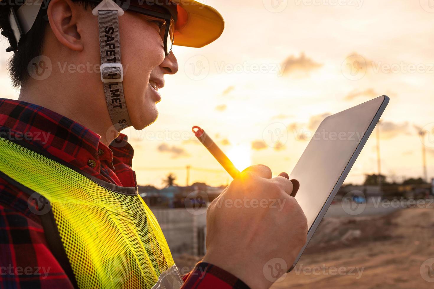 tecnico asiatico ingegnere civile utilizza tablet con tecnologia smart pen sulla costruzione del sito di trasporto per ispezionare il lavoro di ingegneria del progetto online con il team all'ora del tramonto foto