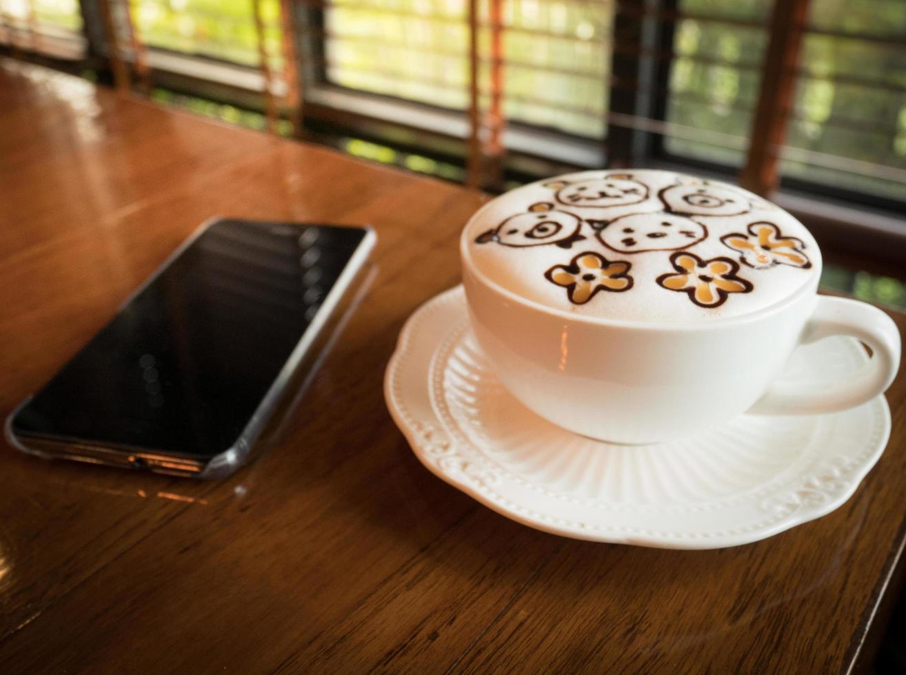 caffè latte art con telefono cellulare con schermo vuoto per la pubblicità, inserire un messaggio o un argomento promozionale presso la caffetteria. foto