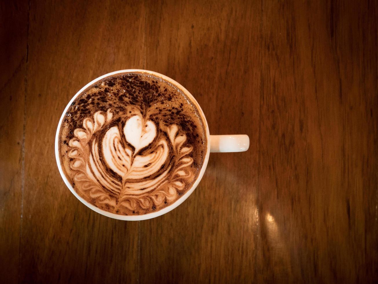 cappuccino con schiuma di latte fresco e latte art in un vetro ceramico bianco su un tavolo di legno in una caffetteria. foto