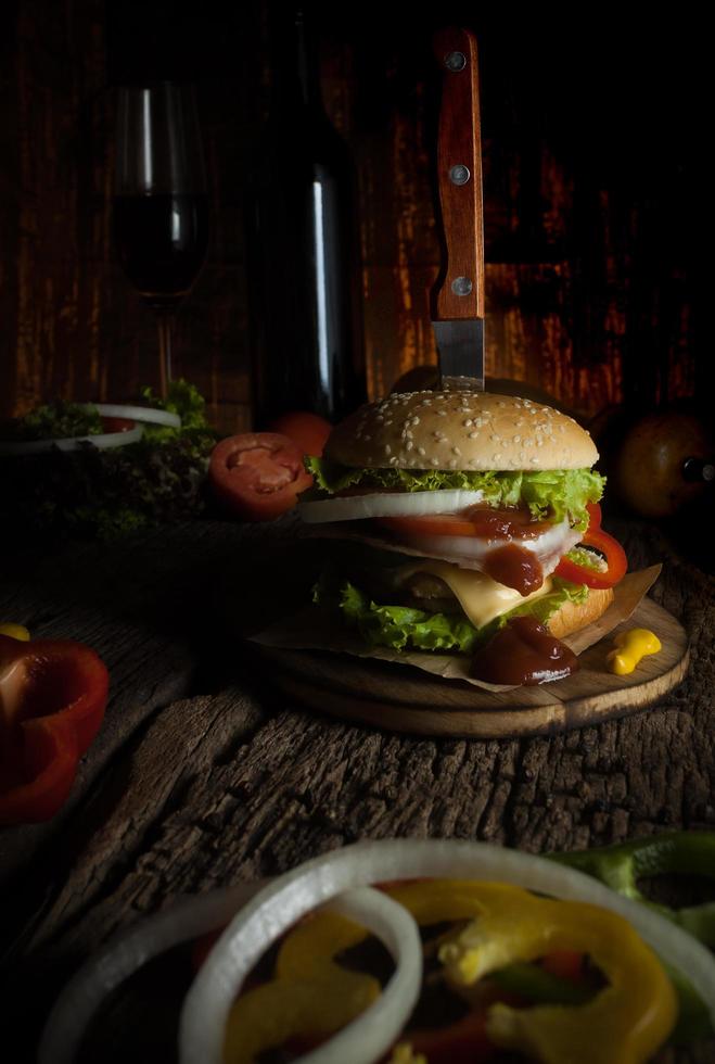 l'hamburger di maiale fatto in casa con pancetta grigliata contiene verdure, formaggio, lattuga, cipolla, peperoncino, spezie in un piatto di legno su un pavimento di legno. foto