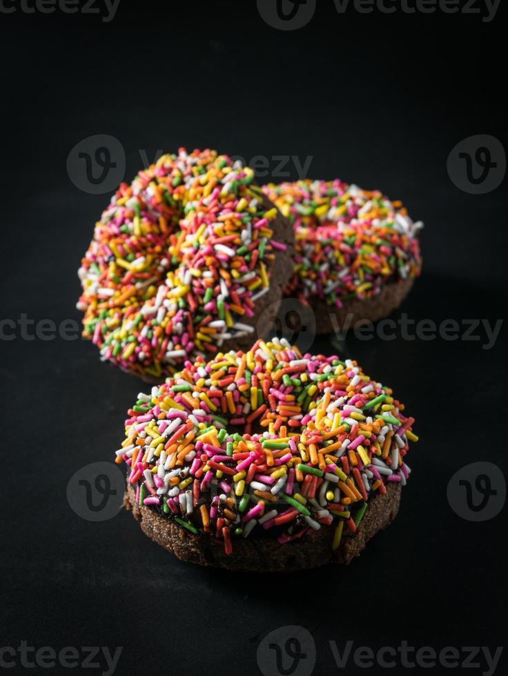 tre ciambelle glassate con granelli colorati isolati su sfondo nero. vista d'angelo. foto