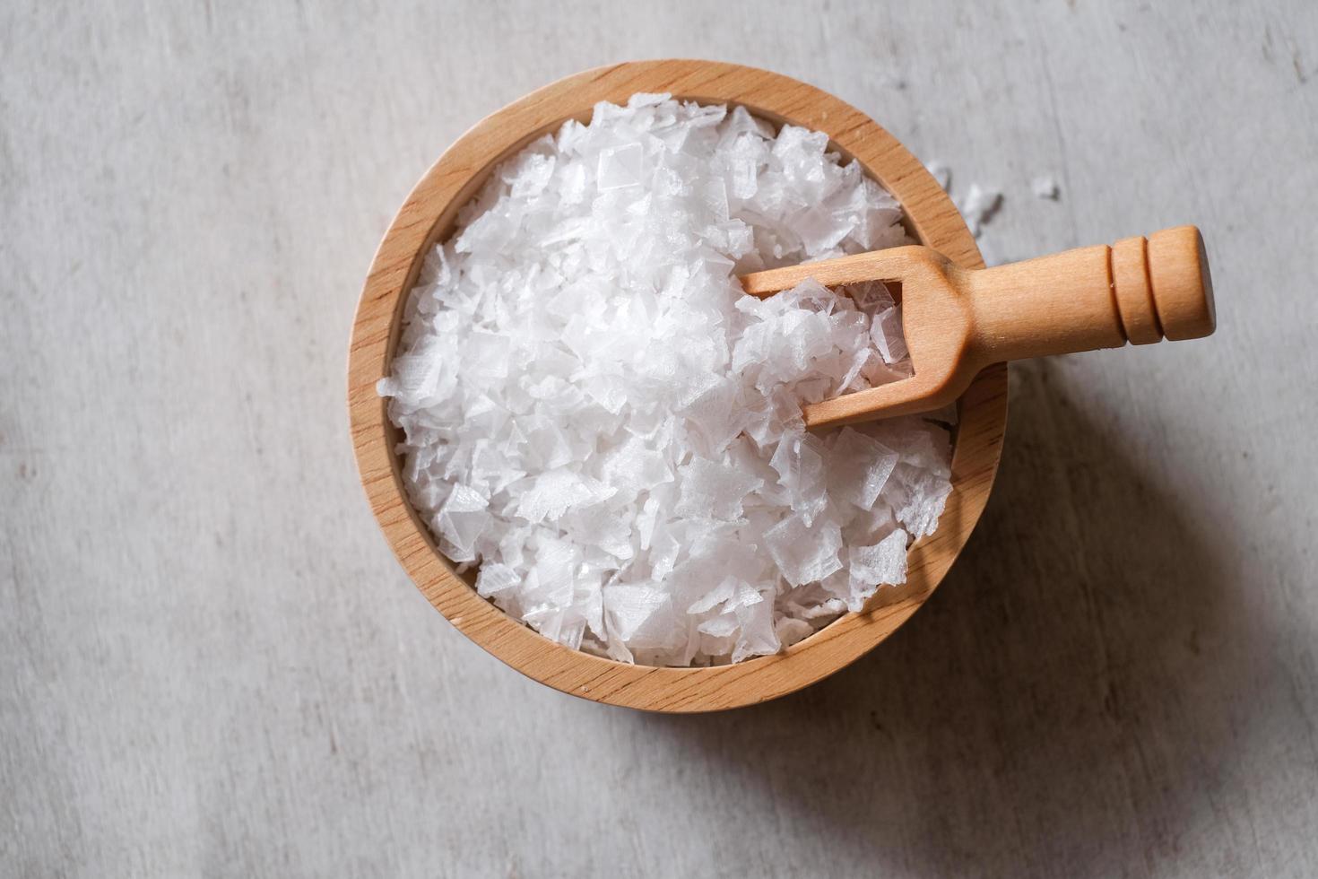 fiore di sale, è un sale che si forma come una crosta sottile e delicata sulla superficie dell'acqua di mare nella paletta di legno e nella ciotola di legno su fondo di legno. messa a fuoco selettiva. foto