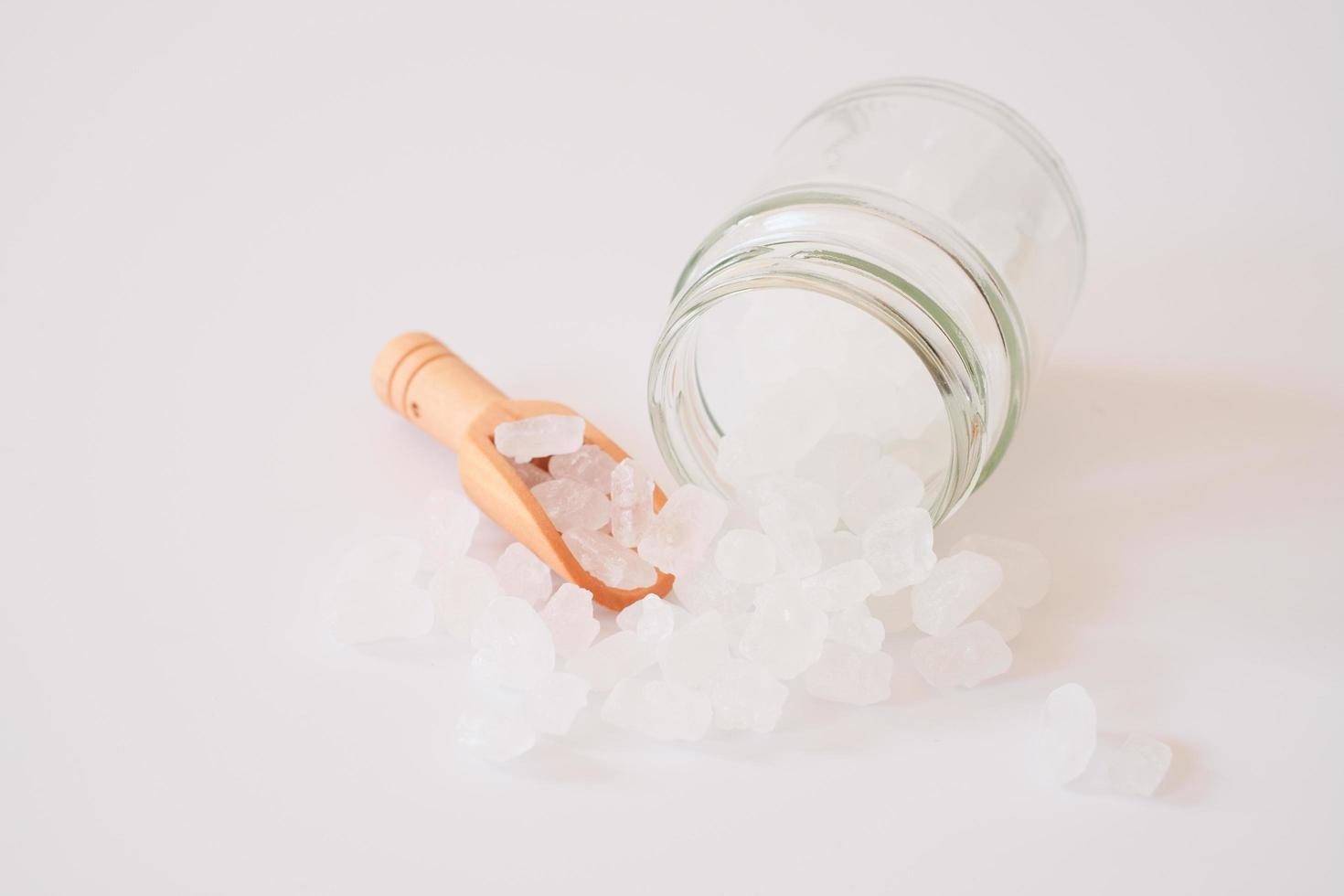 zucchero candito bianco o zucchero cristallino in misurino di legno e barattolo di vetro isolato su sfondo bianco. lo zucchero di roccia bianco viene sciolto e quindi lasciato cristallizzare in una gemma semitrasparente. foto