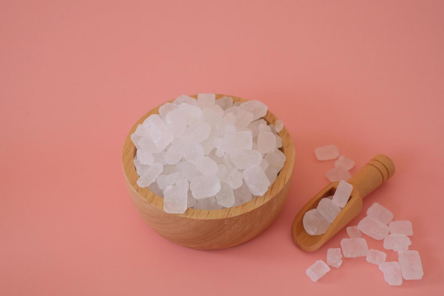 zucchero candito bianco o zucchero cristallino in paletta di legno e ciotola di legno isolata su sfondo bianco. lo zucchero di roccia bianco viene sciolto e quindi lasciato cristallizzare in una gemma semitrasparente. foto
