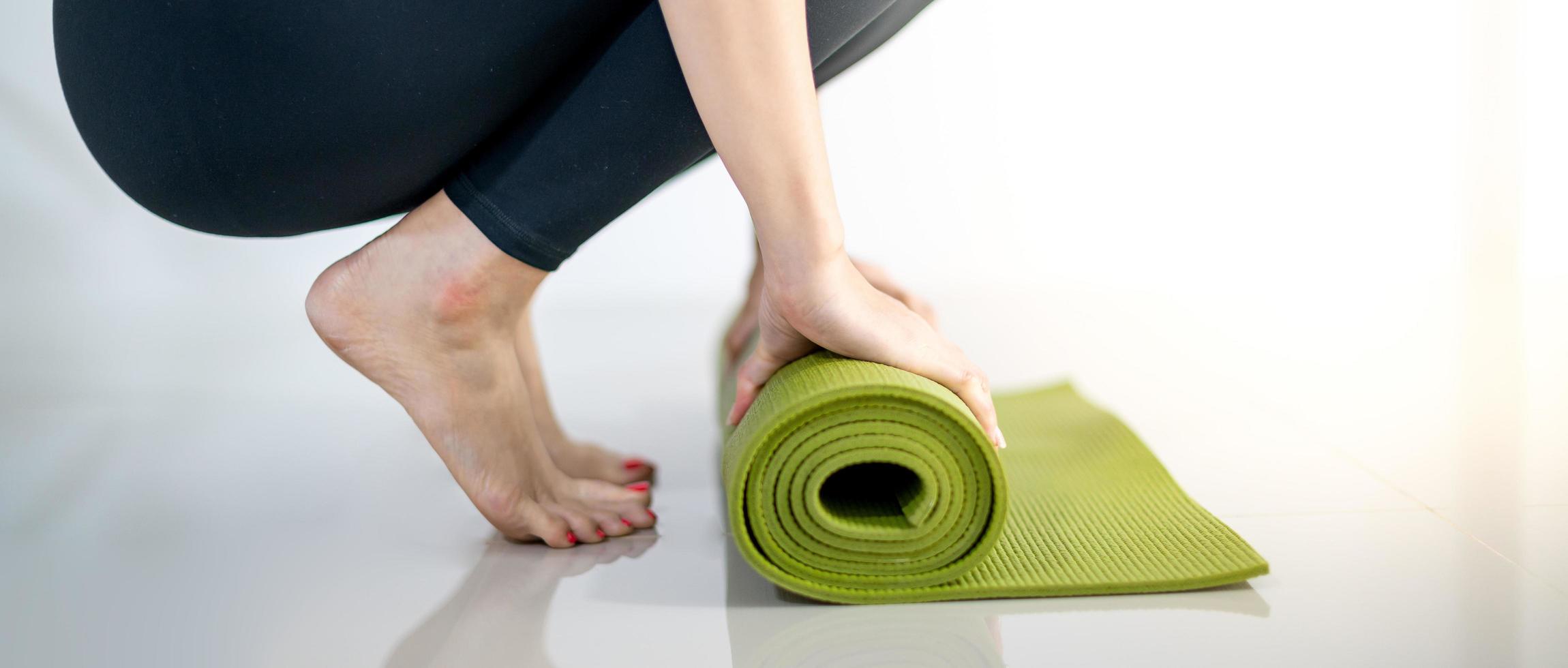 stuoia di yoga verde di rotolamento della mano femminile per preparare l'esercitazione sulla stuoia. foto