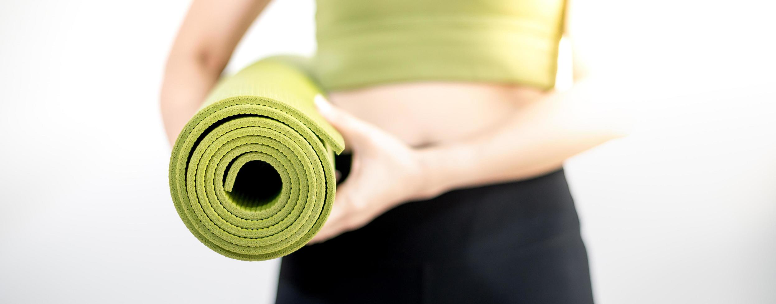 mano femminile che tiene tappetino yoga verde per preparare l'esercizio sul tappetino. foto