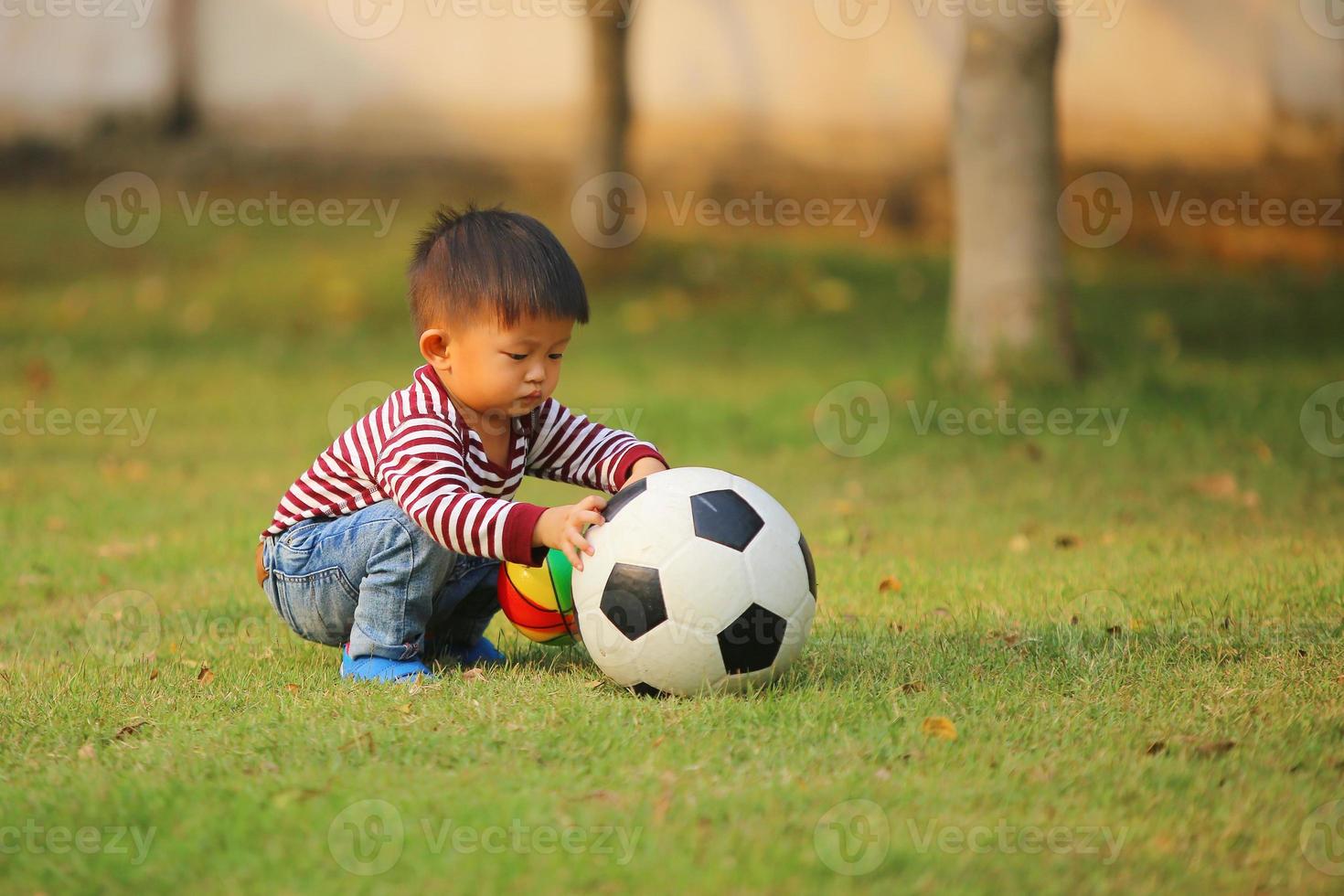 ragazzo asiatico che gioca a calcio al parco. bambino con le palle nel campo in erba. foto