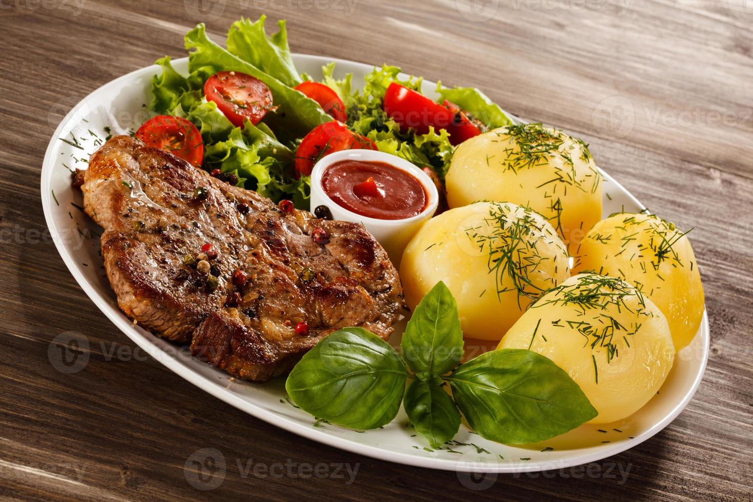 bistecca alla griglia, patate lesse e verdure su fondo di legno foto